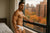 AI-generated image of a gay man in white underwear standing by a window with a cityscape view in his jockstrap